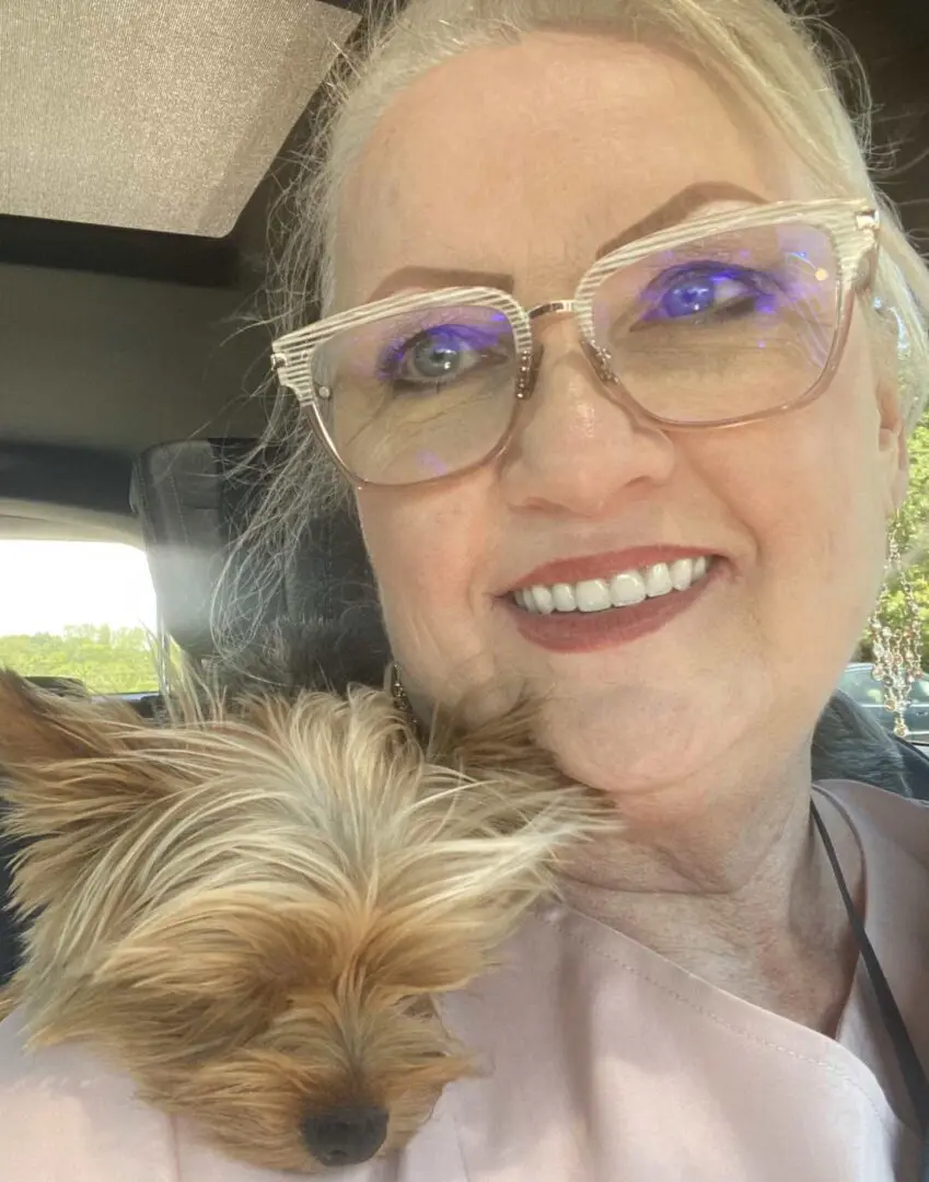 A woman with glasses and a dog in the back of a car.
